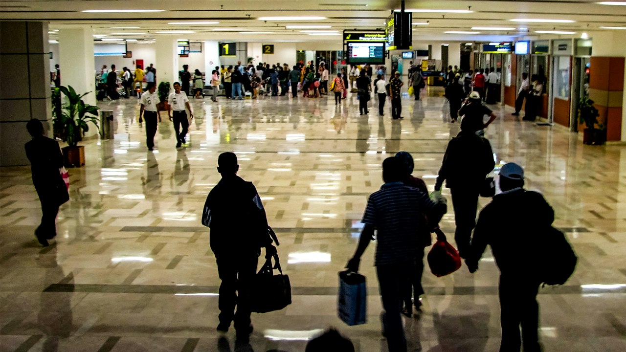 Travellers walking through an airport concourse with wheeled luggage